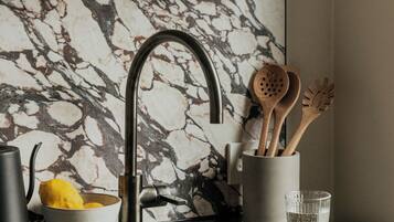 A kitchen with a marble backsplash, a modern faucet, and wooden utensils in a holder.
