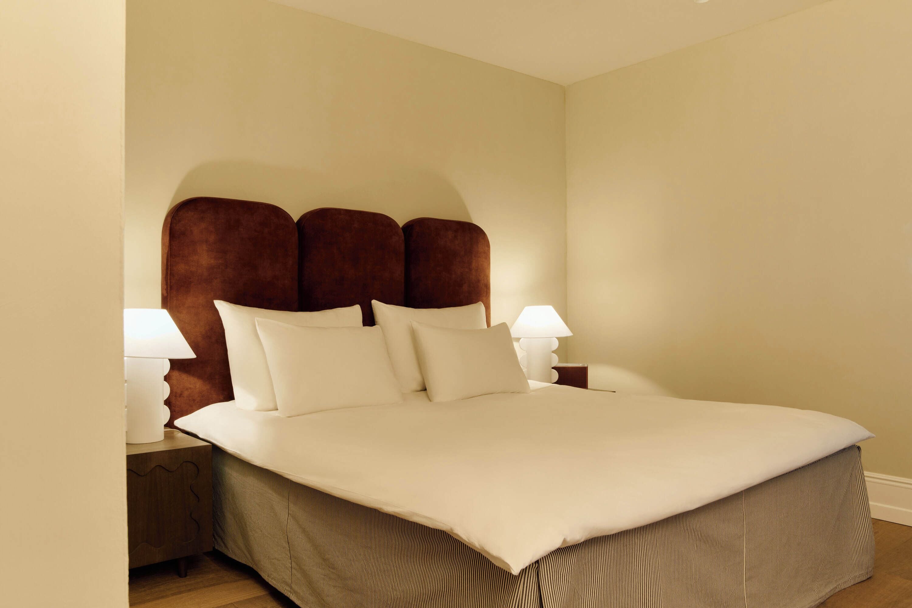 A neatly made bed with a brown headboard, white bedding, and two bedside lamps.