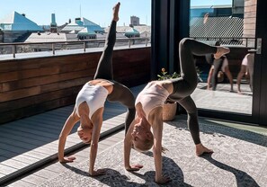 Two people performing a handstand on a wooden deck with a view of buildings in the background. - Revier (Oslo)