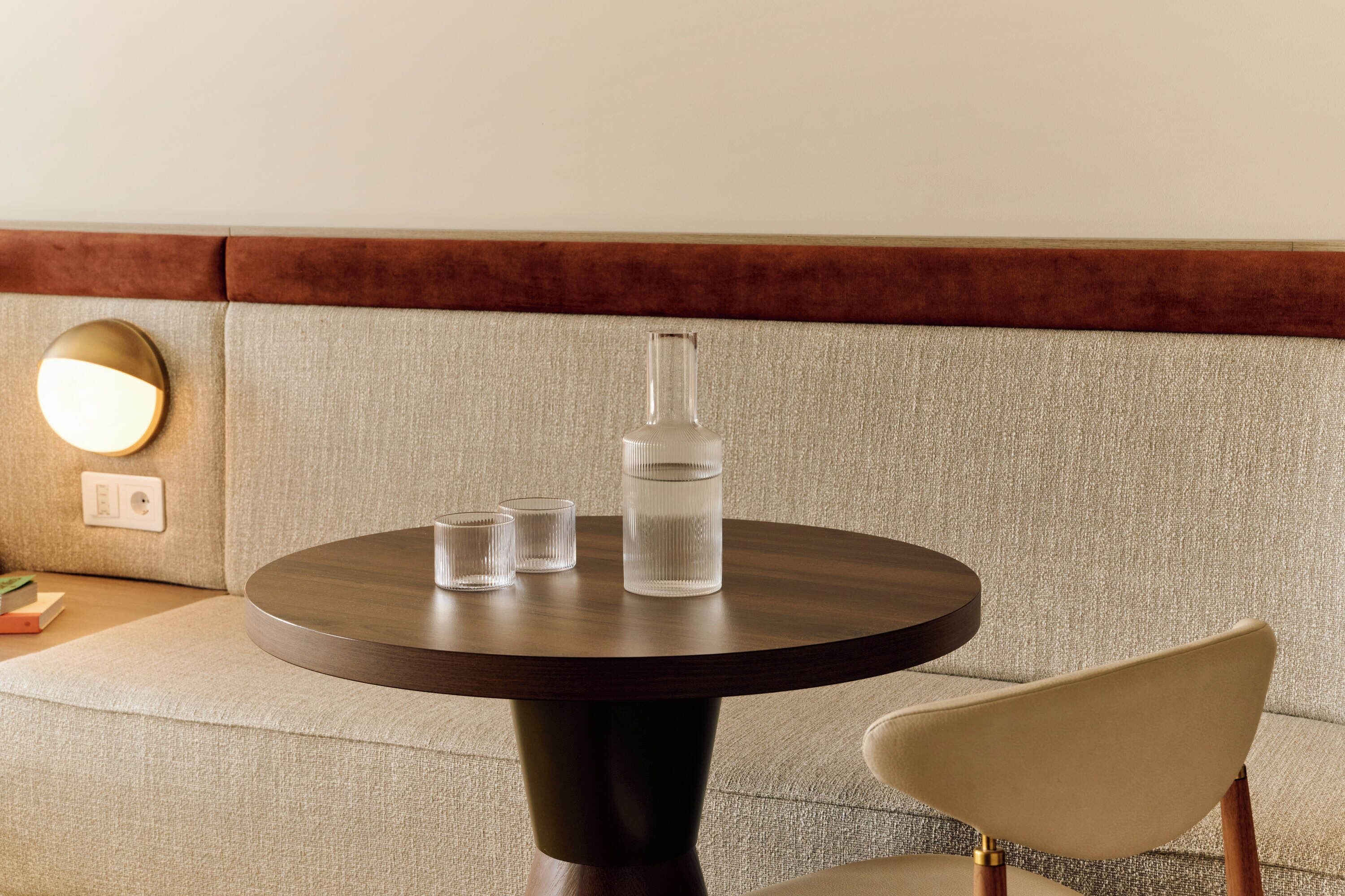 A round table with a dark wooden base, a clear glass bottle, and two clear glasses on a beige upholstered sofa.