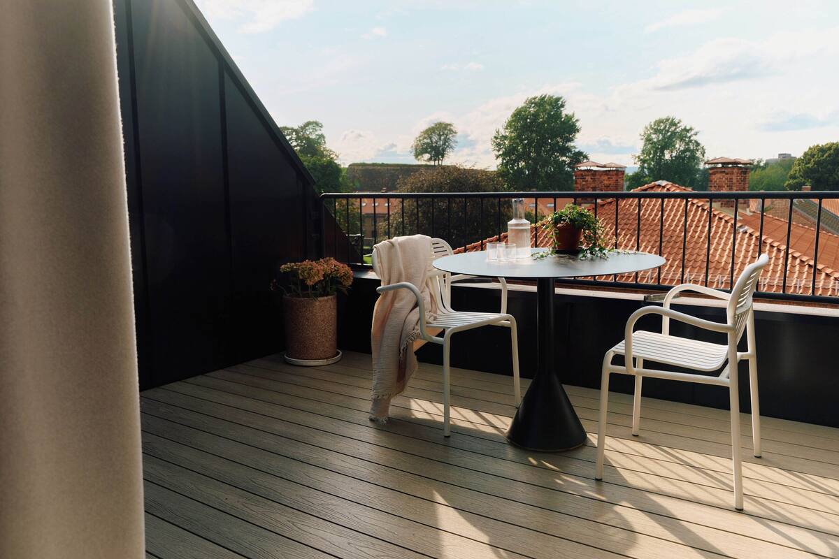 A wooden deck with a round table and two white chairs, a potted plant, and a black chair.