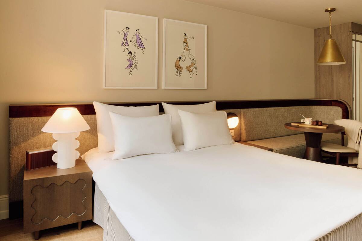 A hotel room with a large bed, two bedside tables, a round table, and artwork on the wall.