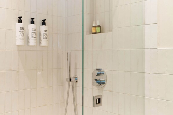 Un baño con paredes de azulejos blancos, puerta de cristal para la ducha y tres botellas de acondicionador D&S URGA en la pared.