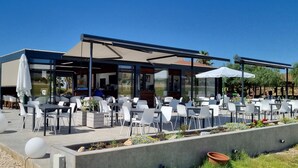 An outdoor dining area with tables and chairs, a covered seating area, and a view of the surrounding landscape.