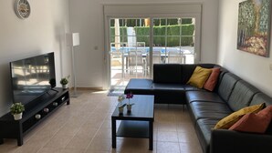 A living room with a black leather sofa, a coffee table, a TV, and a sliding glass door leading to an outdoor area with a pool and chairs.