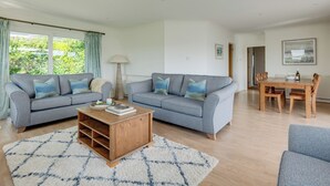 A living room with two grey sofas, a wooden coffee table, and a dining table with chairs.