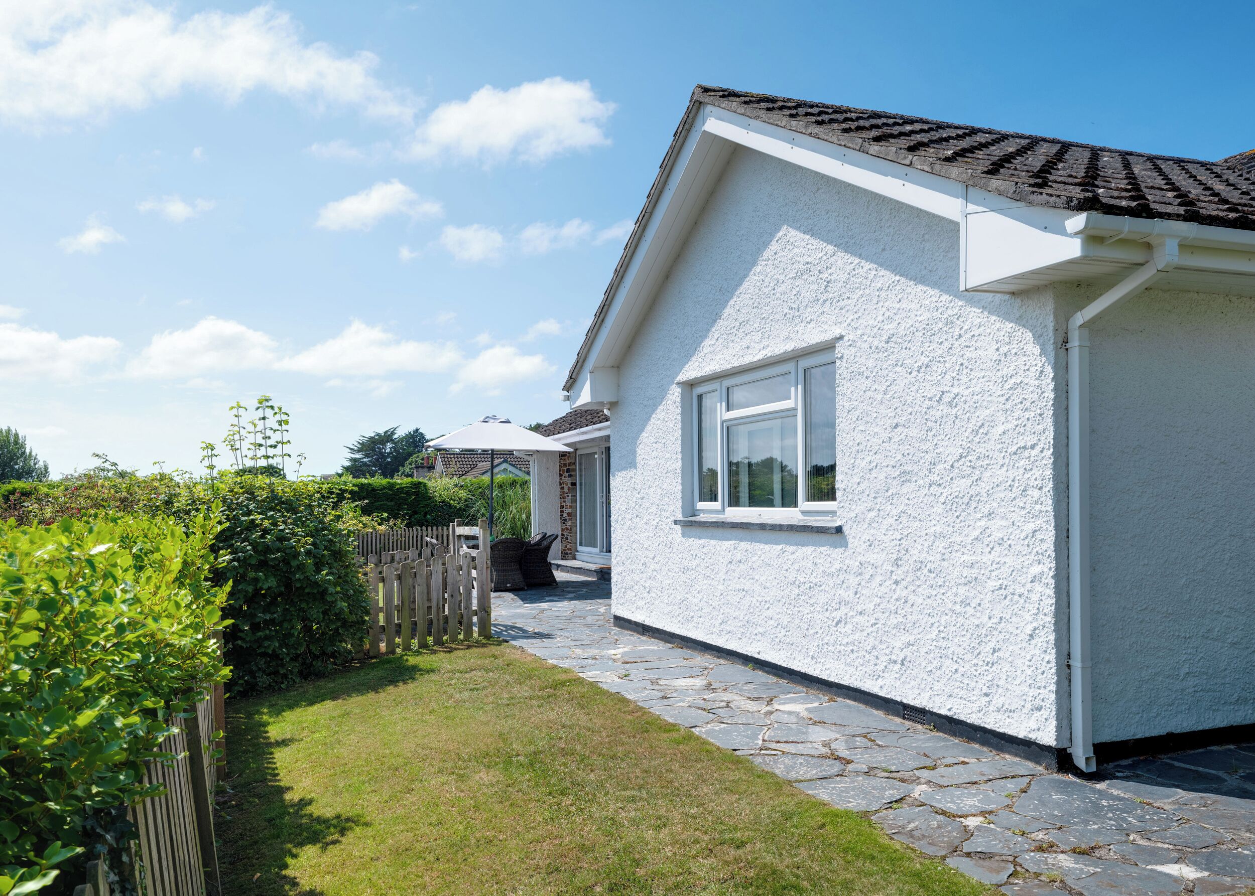 A white house with a tiled roof, a stone pathway, and a wooden fence.