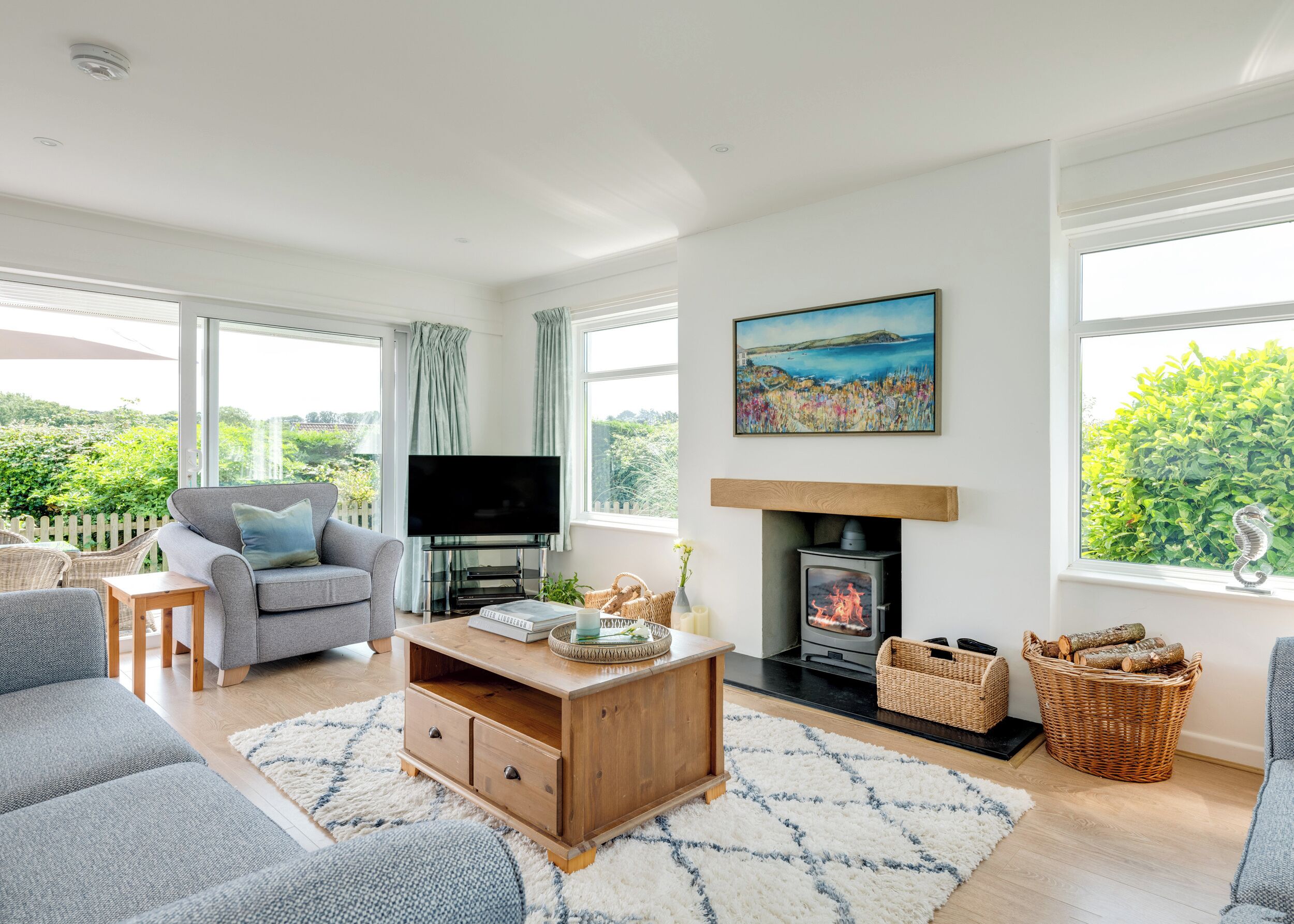 Uma sala de estar moderna com lareira, TV de tela plana e um quadro de uma paisagem costeira.