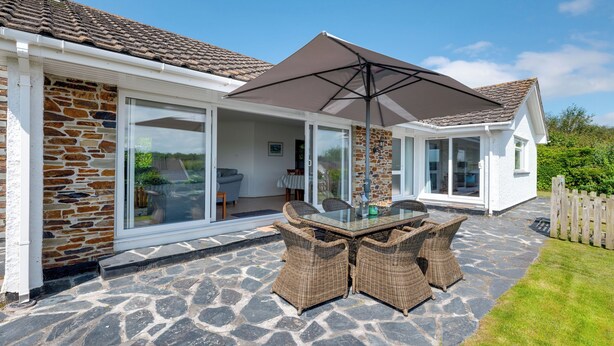 A house with a stone exterior, a glass door leading to a patio, and a covered outdoor seating area with a table and chairs.