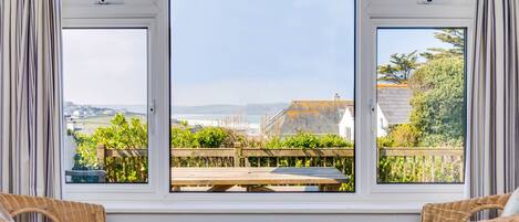 Una habitación con un ventanal grande que da a un jardín y vistas al mar. Hay sillones de mimbre y una mesa en la habitación.