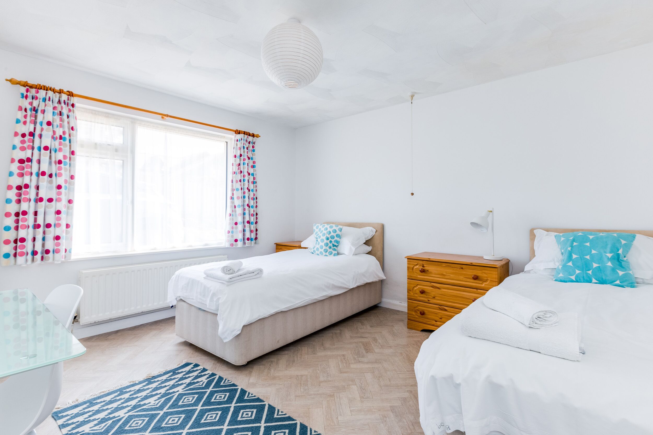 Een slaapkamer met twee bedden, een houten dressoir, een glazen tafel en een kamerkleed met dessin.