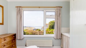 Ein Schlafzimmer mit großem Fenster, einem hölzernen Schminktisch, Heizkörper und Blick ins Grüne.