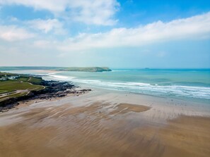 A coastal landscape with a beach, rocky shoreline, and distant hills.