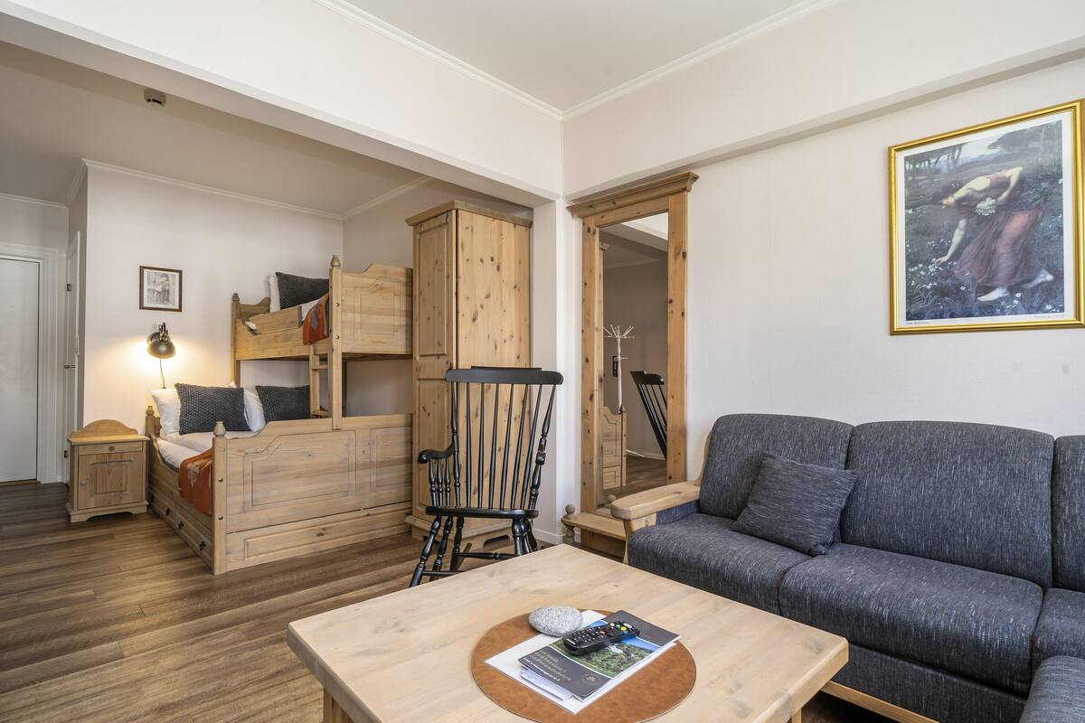Ein gemütliches Zimmer mit einem Etagenbett, einer Schlafcouch, einem Holztisch und einem gerahmten Bild an der Wand.