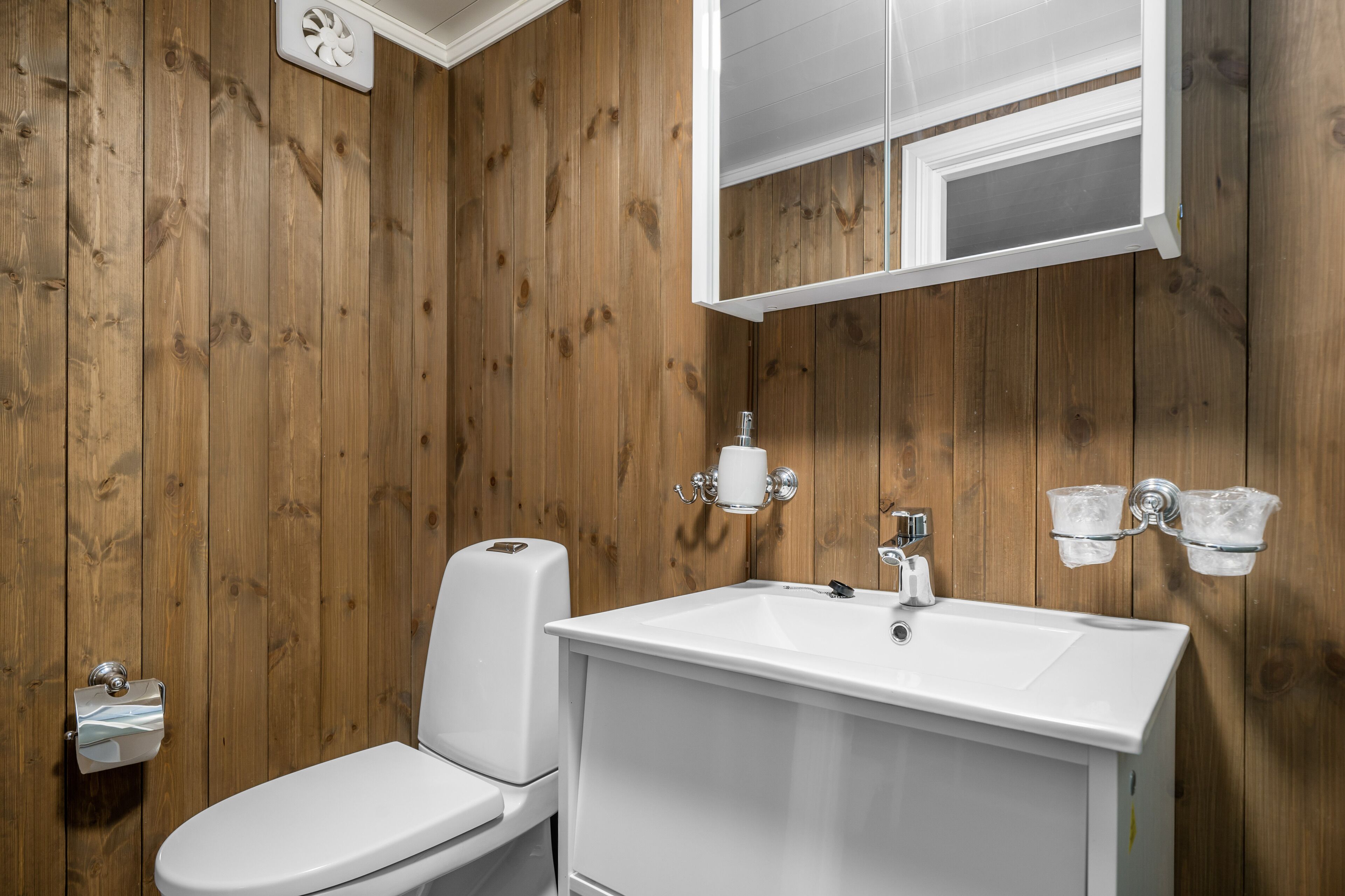 A bathroom with wooden walls, a white toilet, a sink, and a mirror.