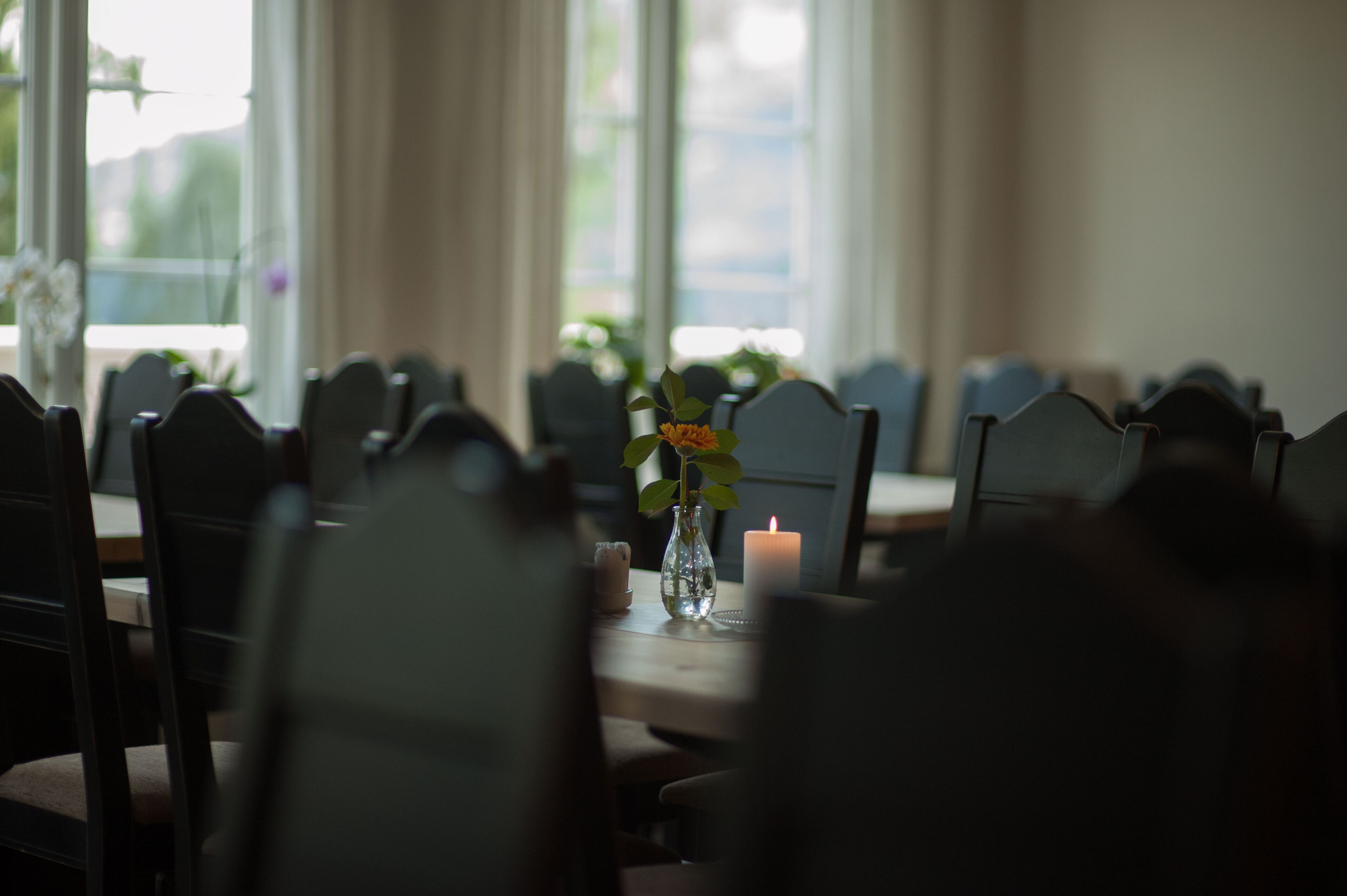 A dining table with chairs, a candle, and a vase with flowers.