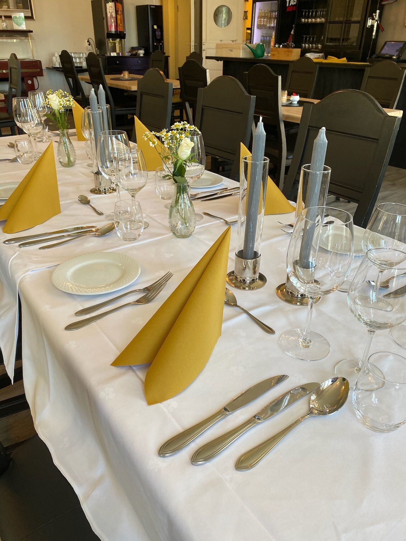A table set for a formal dinner with white tablecloths, gold napkins, and clear glassware.