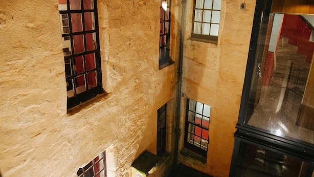 Un couloir étroit avec un mur à texture et de nombreuses fenêtres munies de barreaux en métal.