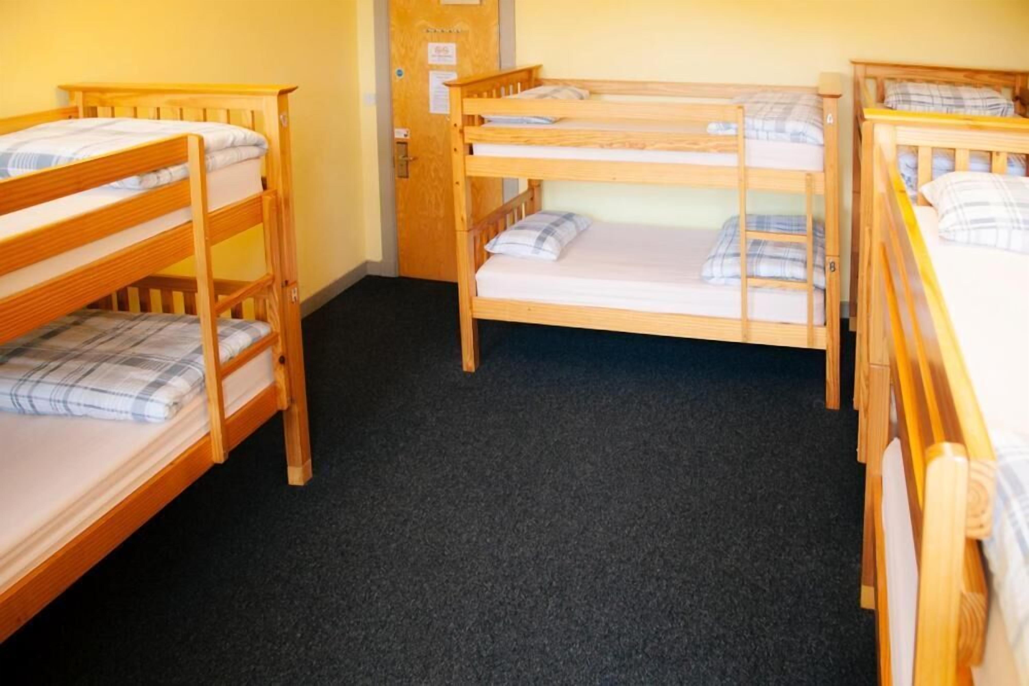 A room with four bunk beds, wooden headboards, and a carpeted floor.