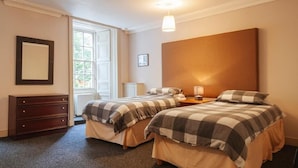 Une chambre avec deux lits, une commode, une fenêtre et une lampe.
