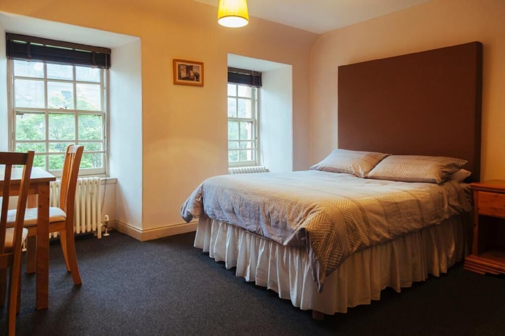Quarto com cama, cadeira, escrivaninha e duas janelas.
