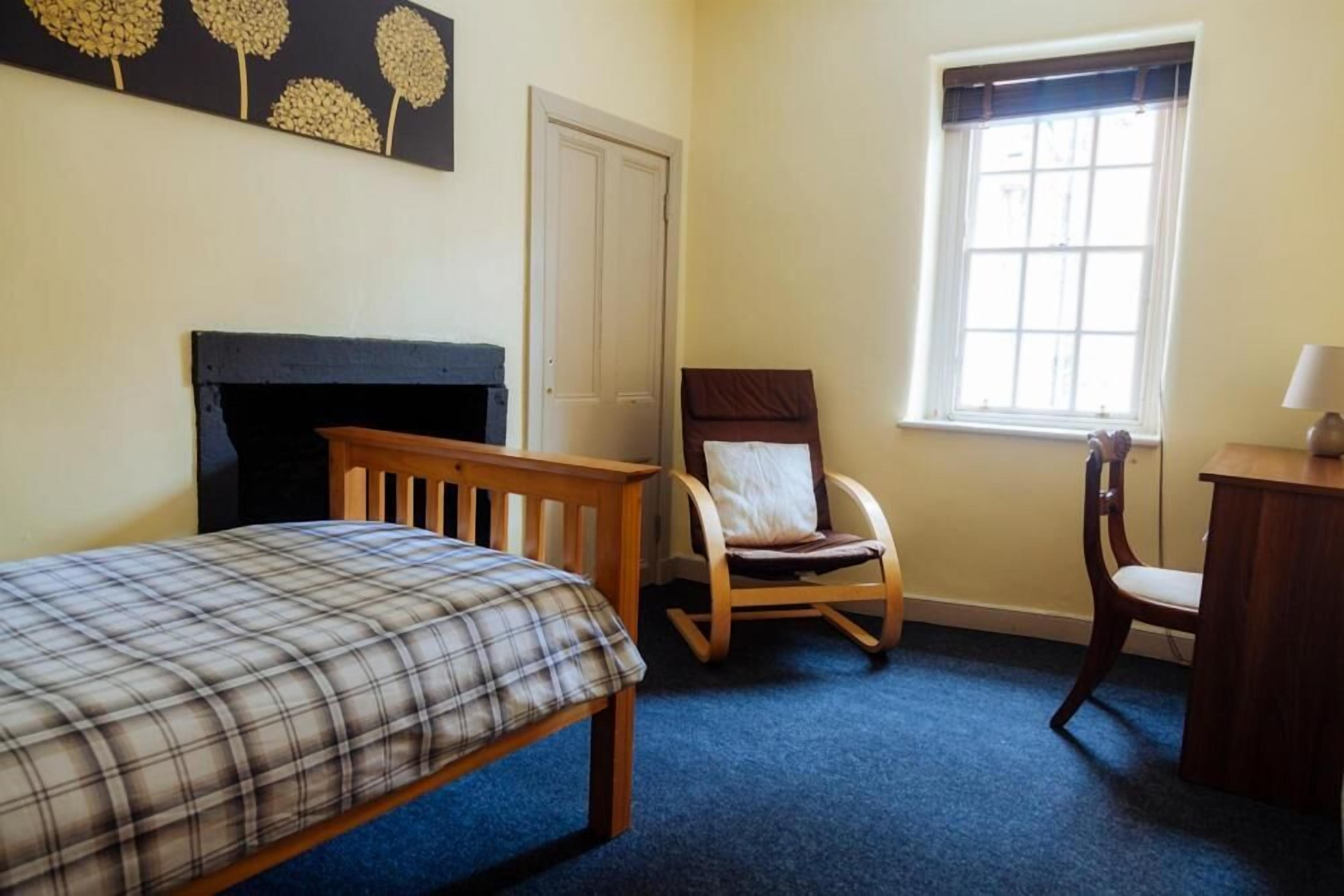 Ein Schlafzimmer mit einem Bett, einem Holzstuhl, einem Schreibtisch, einem Kamin und einem Fenster.