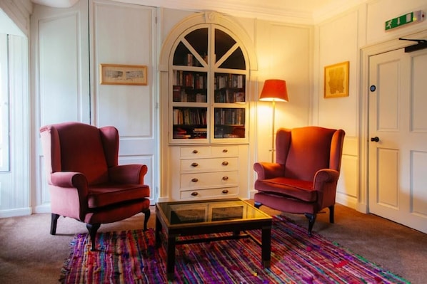Una habitación con dos sillones rojos, una mesa de centro de vidrio, una estantería y una alfombra estampada.