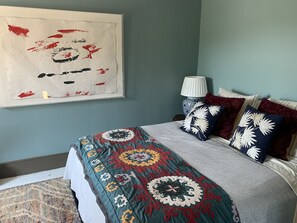 Un dormitorio con cama, un cuadro en la pared, una lámpara de noche y almohadas estampadas.
