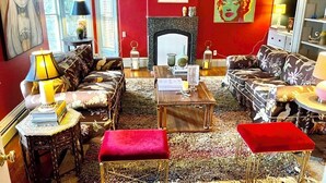A living room with red walls, a fireplace, and various pieces of furniture including a sofa, armchairs, and a coffee table. - Spacious Adirondacks Retreat • 6BR, Heated Pool. Lake Champlain  (Willsboro)