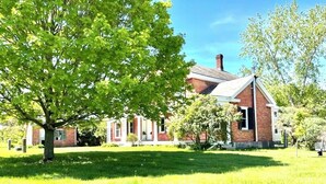 A brick building with a large tree in the foreground. - Spacious Adirondacks Retreat • 6BR, Heated Pool. Lake Champlain  (Willsboro)