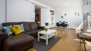 Un salon moderne avec un canapé en cuir marron, une table basse blanche agrémentée d’une plante, et un coin repas avec une table et des chaises blanches.