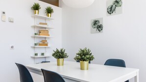 Un coin repas avec une table blanche, des chaises bleu foncé et des étagères dorées ornées de plantes et de livres.