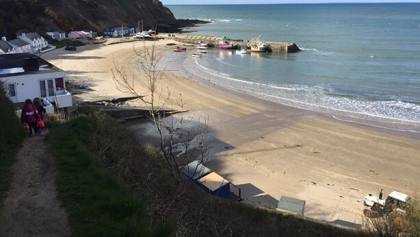 Ein Küstenstrand mit sandigem Ufer, einigen Booten und einer felsigen Klippe.