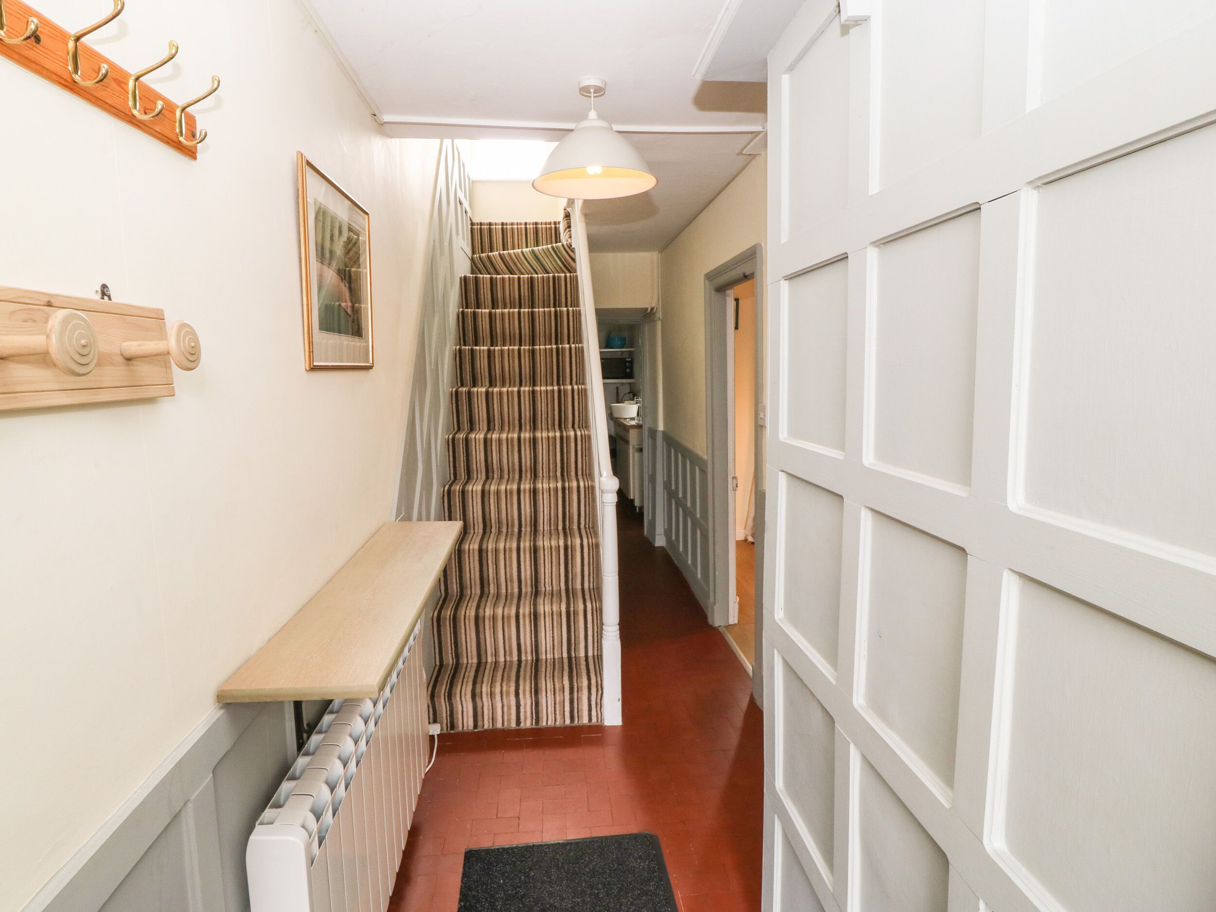 A narrow hallway with a wooden bench, a radiator, a striped staircase, and a door with a white panel.