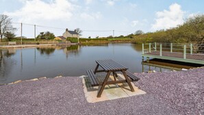 Ein Picknicktisch an einem ruhigen Gewässer, eine hölzerne Bank und eine kleine Brücke.