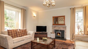 A living room with a sofa, a coffee table, a flat-screen TV, a fireplace, and a chandelier. - Old Manse (Muir of Ord)