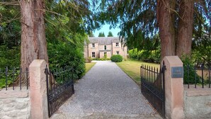 A gravel driveway leading to a stone building with a black iron gate labeled "Old Manse." - Old Manse (Muir of Ord)