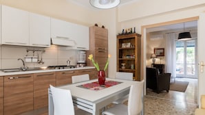 Een moderne keuken met witte kasten, een eettafel met stoelen, een vaas met bloemen en een houten boekenkast.