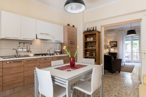 Une cuisine moderne avec des meubles blancs, une table à manger avec des chaises, un vase rempli de fleurs et une bibliothèque en bois.