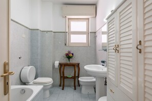 A compact bathroom with a toilet, bidet, sink, and bathtub.