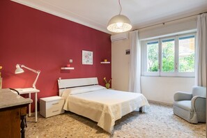 A bedroom with a bed, bedside table, lamp, chair, and a window with curtains.