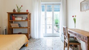 Een slaapkamer met een bed, een houten bureau, een boekenkast en uitzicht door een glazen deur op een buitengebied.