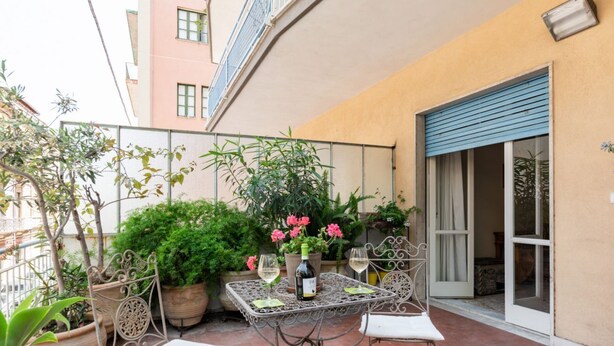 Een terras met een tafel, stoelen, potplanten en een fles wijn.