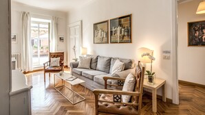 A living room with a sofa, armchairs, a coffee table, and a side table with a lamp. There are framed pictures on the wall and a window with curtains. - Dolcevita Terrace (Roma)