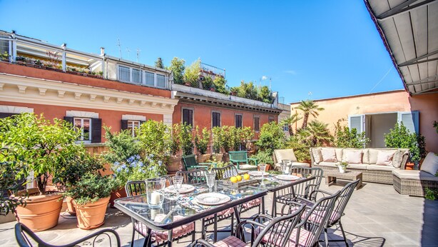 An outdoor patio with a glass table, chairs, and potted plants. - Dolcevita Terrace (Roma)