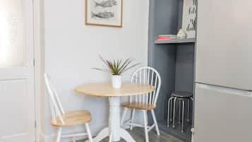 Un pequeño comedor con una mesa redonda, dos sillas, una planta en maceta y una obra de arte enmarcada en la pared.