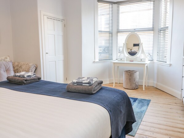 A bedroom with a bed, a vanity with a mirror, and a window with blinds.