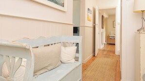 A hallway with a wooden bench, a painting on the wall, and a door leading to another room. - Sandy Lodge Rock (Wadebridge)