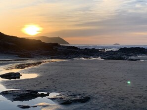 Una playa con terreno rocoso y un atardecer de fondo.