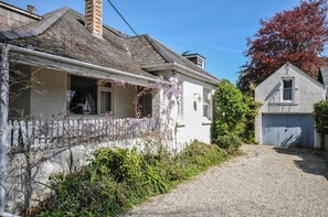Una casa de dos pisos con camino de grava, cerca de piquetes blancos y un jardín con flores moradas.